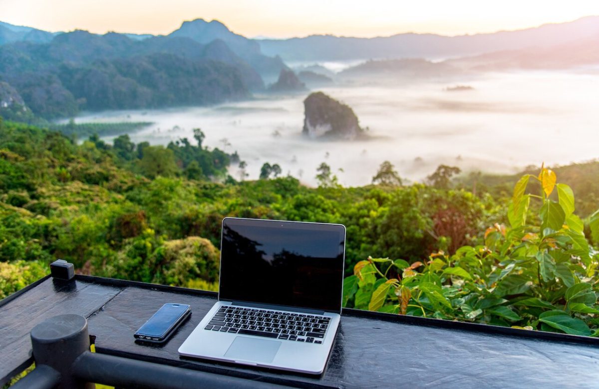 A laptop, mobile on wooden table with sunrise and mountain fog background in morning. A start of new day. Freelance business concept.