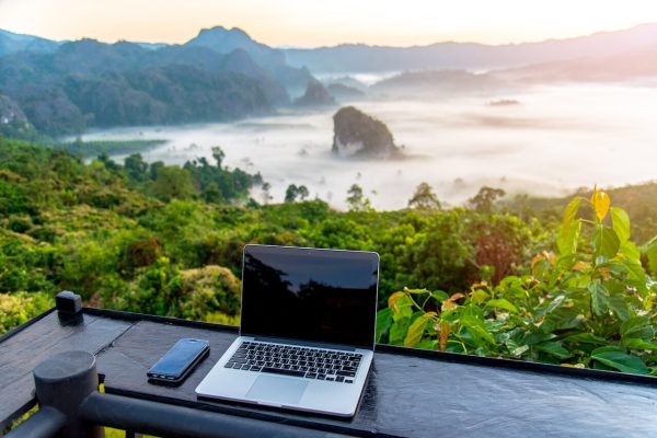 A laptop, mobile on wooden table with sunrise and mountain fog background in morning. A start of new day. Freelance business concept.