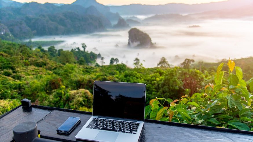 A laptop, mobile on wooden table with sunrise and mountain fog background in morning. A start of new day. Freelance business concept.